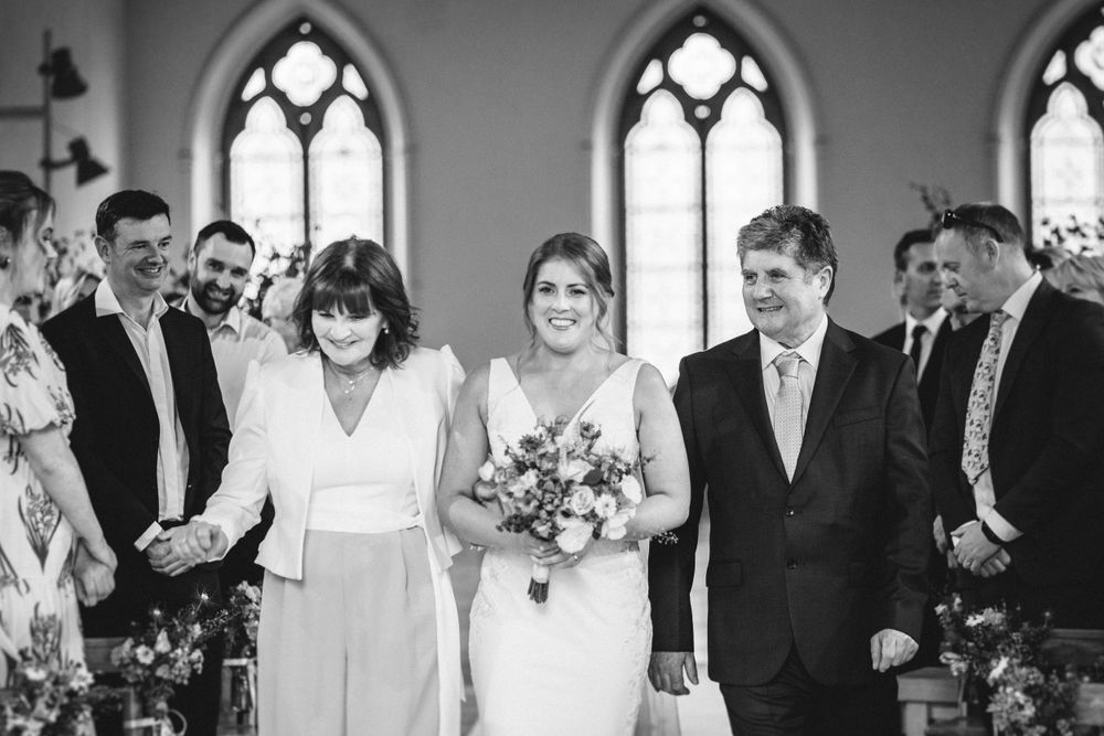 Wedding ceremony in a chapel with gothic windows and brick walls as guests stand together in formal attire.