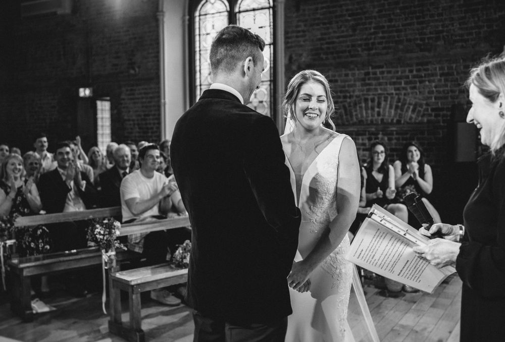 Black and white wedding ceremony photo in brick chapel with elegant arched windows.