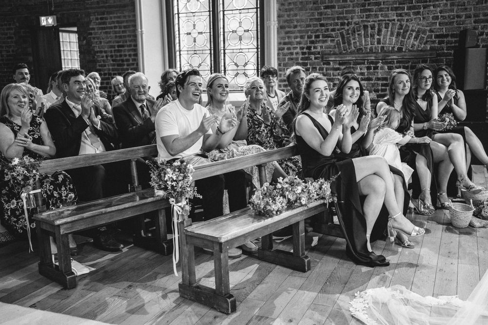 Wedding guests seated on wooden pews in historic brick church during ceremony.
