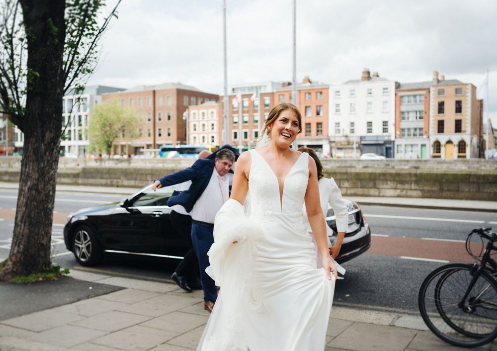 Wedding day shot of person in white dress by car on city street.