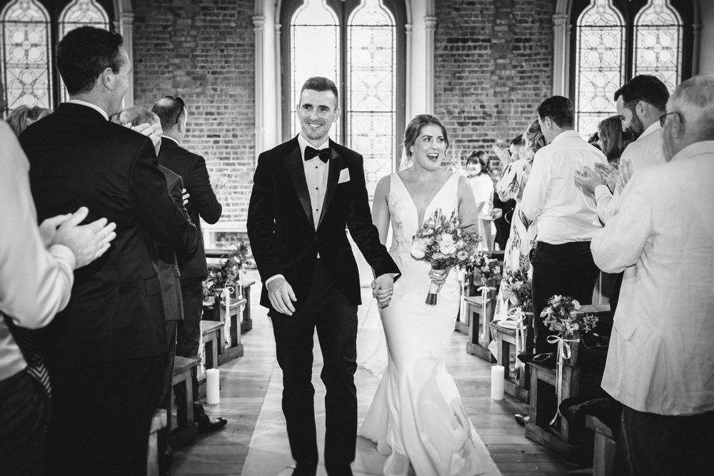 Newlyweds walking down church aisle as guests applaud during recessional.