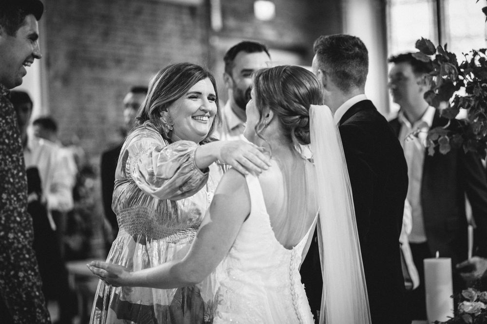Wedding guests celebrating and embracing at an indoor brick-walled venue.