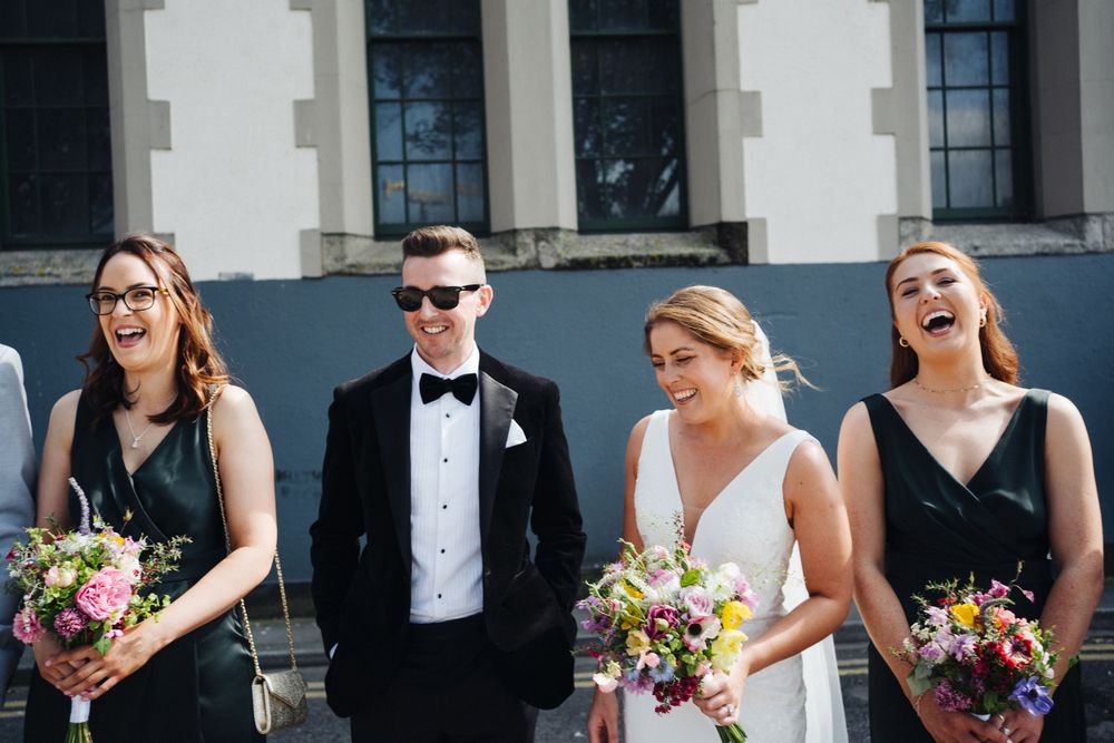 Wedding party poses outdoors in formal attire with colorful bouquets.