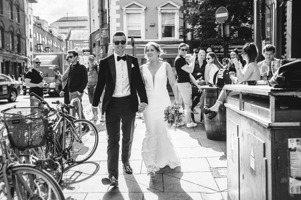 Newlyweds walking through a historic city street lined with bicycles.