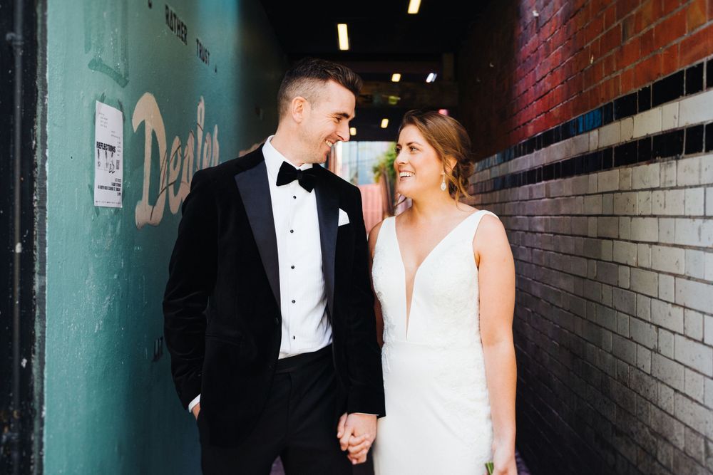 Couple in formal wedding attire sharing a moment in an urban alley.