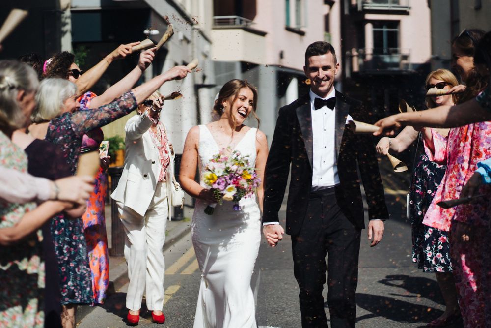 Wedding couple walking through crowd as guests celebrate with confetti.