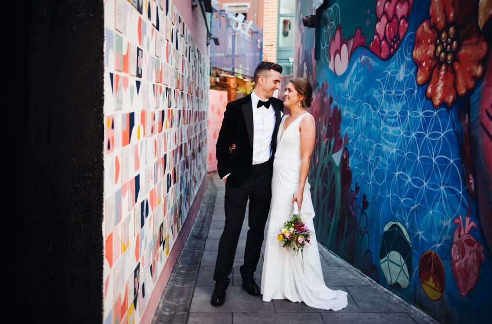 Couple standing against colorful street art mural with floral designs.