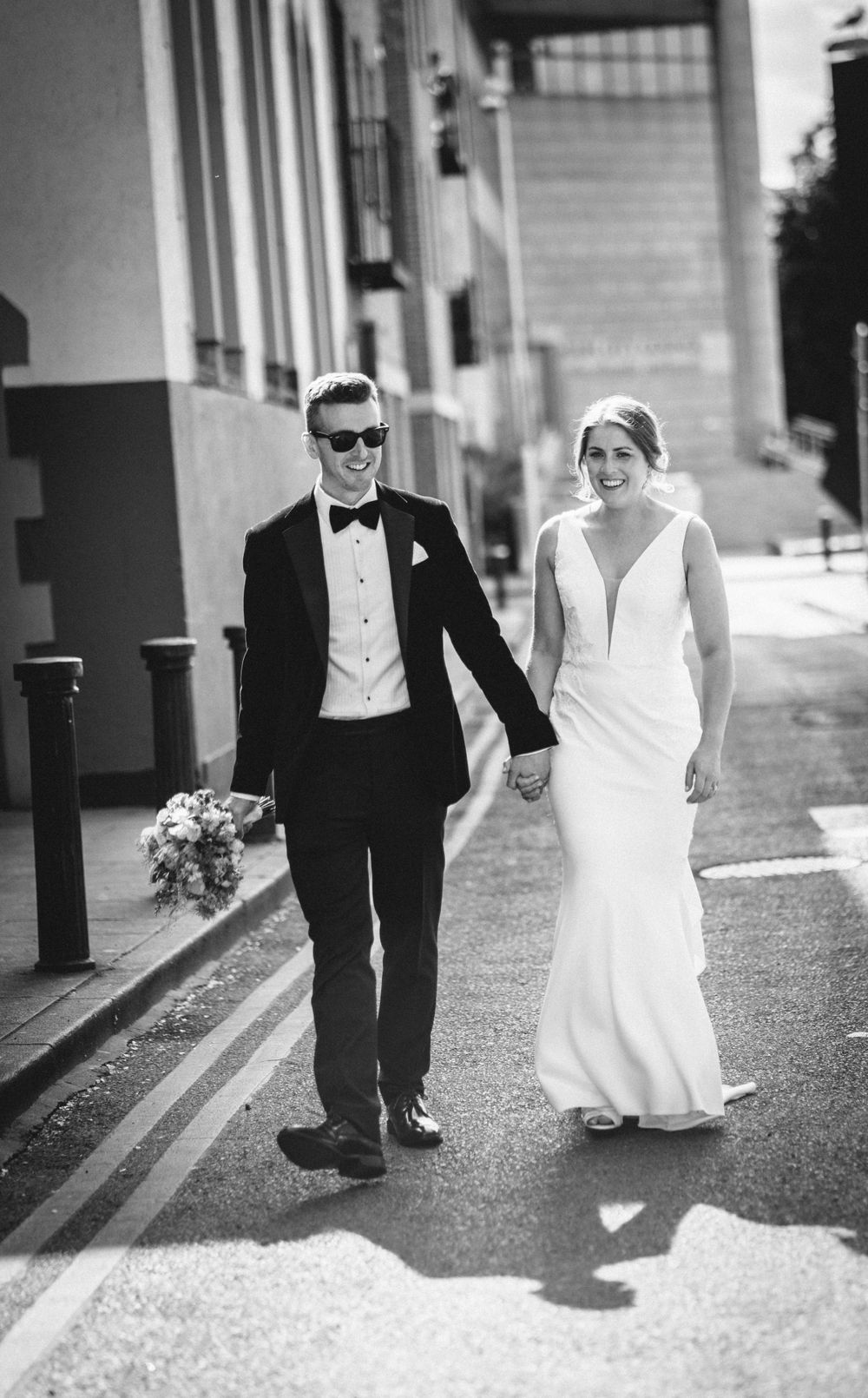 Black and white photo of newlyweds walking hand in hand down a city street.