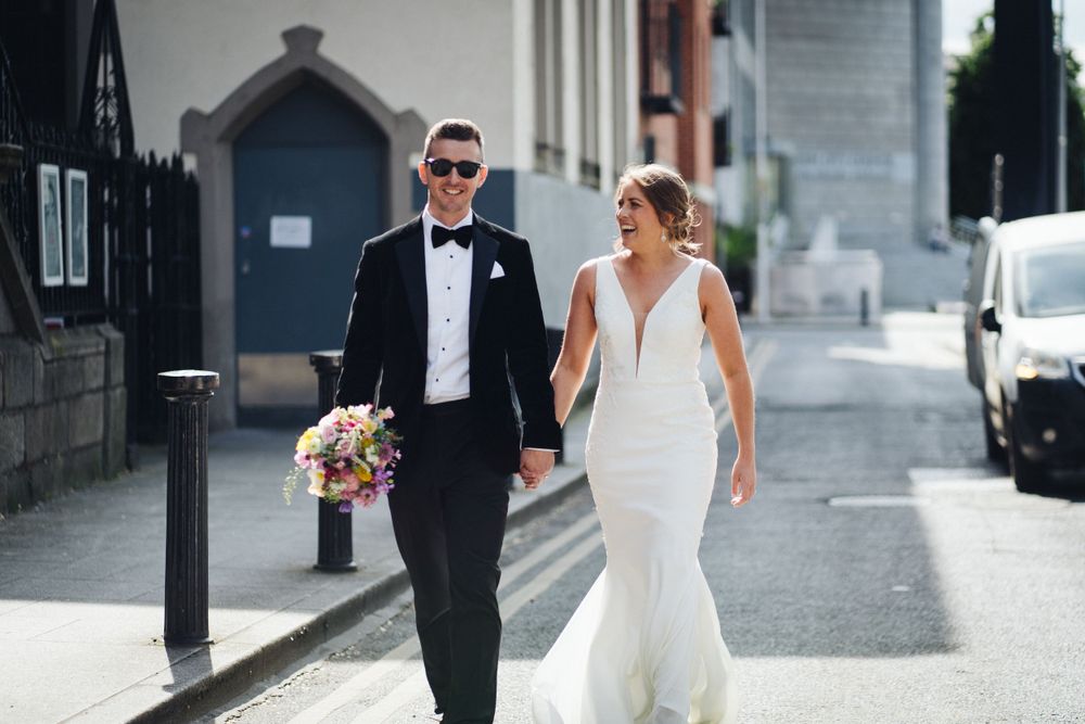 Stylish wedding couple walking together on urban street with bride holding colorful bouquet.