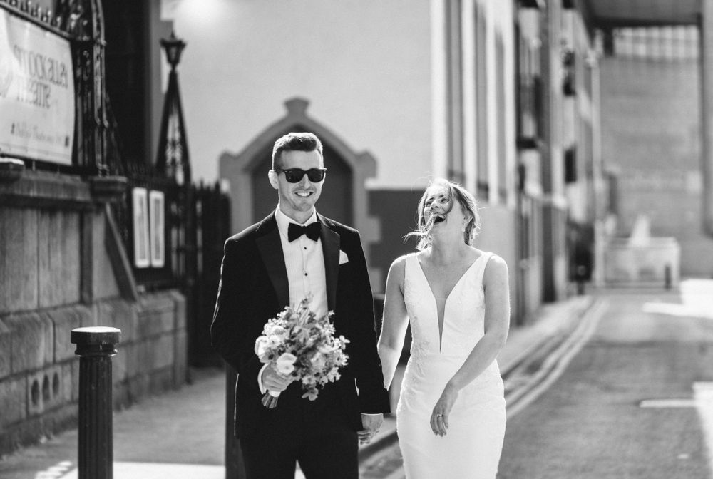 Black and white portrait of wedding couple walking along city street with vintage architecture.