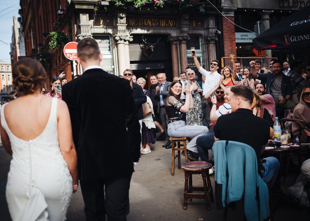 Wedding couple passing by outdoor cafe with crowd of onlookers and well-wishers.