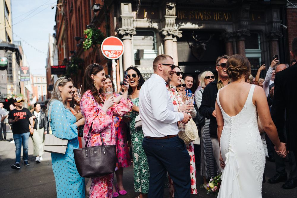 Celebratory scene of wedding guests cheering for couple on busy city street.
