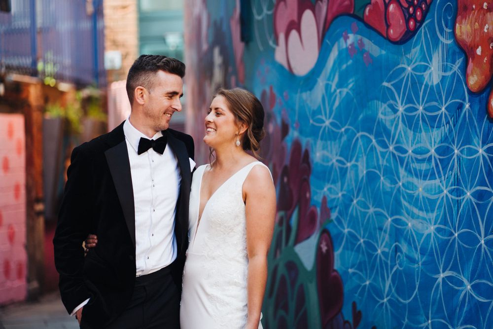 Wedding couple pose against vibrant street art wall with modern urban feel.