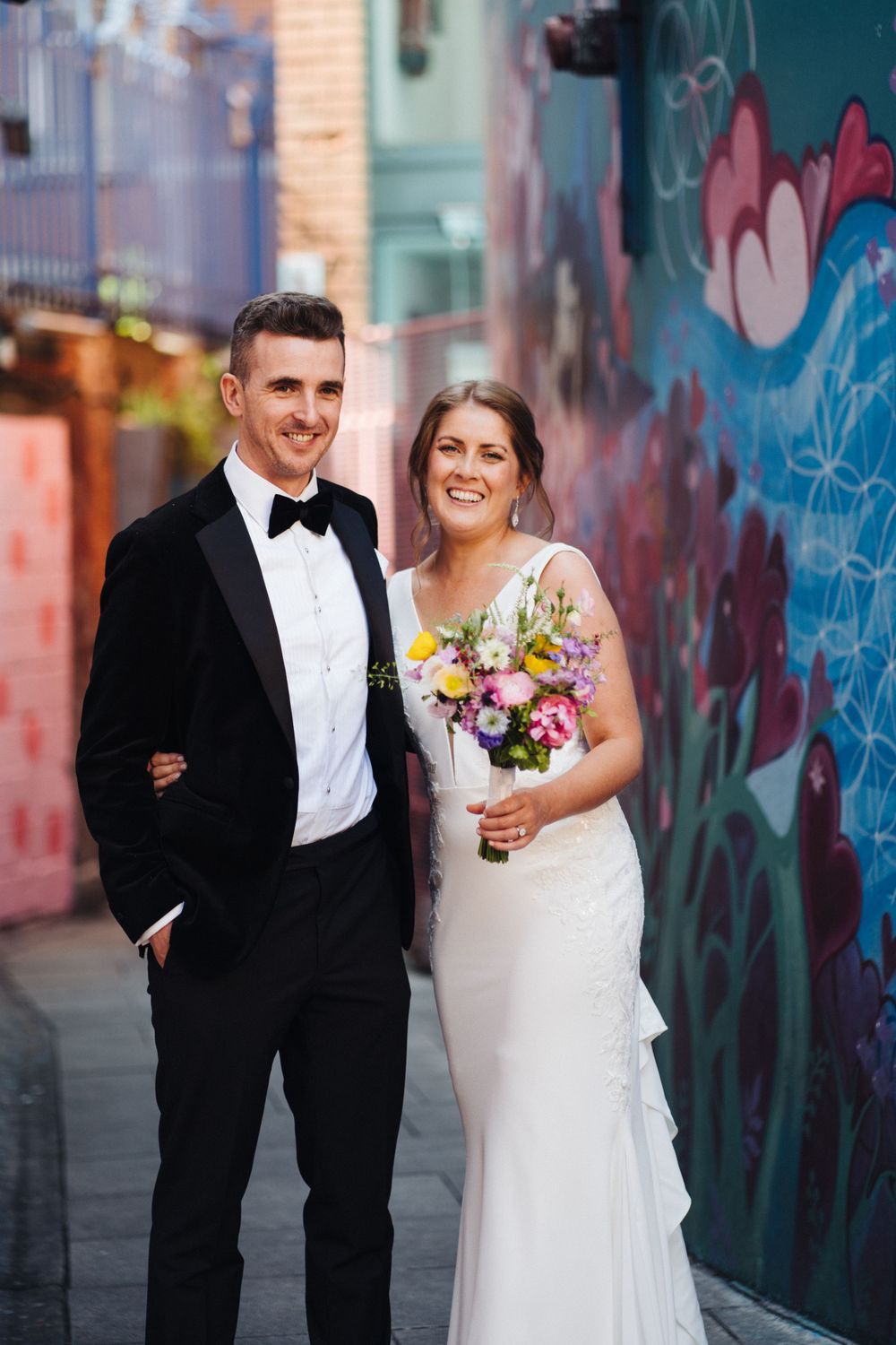Elegant wedding portrait with couple standing by colorful urban mural background.