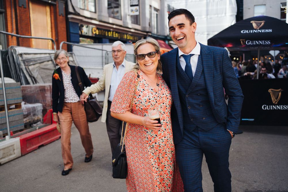 Wedding guests dressed in formal attire socialize on a city street.