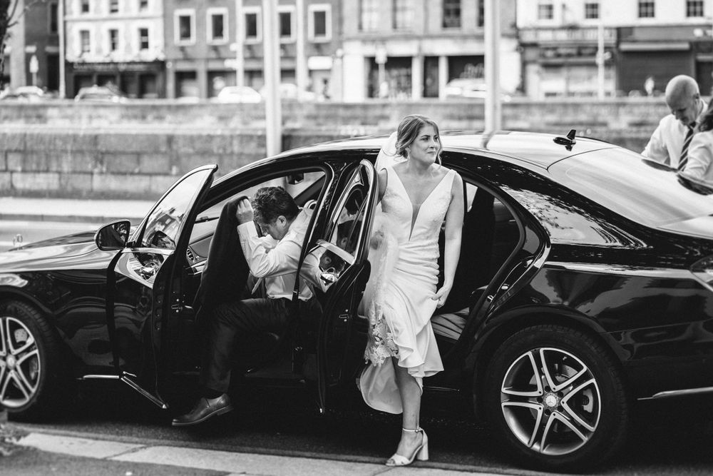 Elegant black luxury sedan with open doors parked in front of historic city buildings on a sunny day.