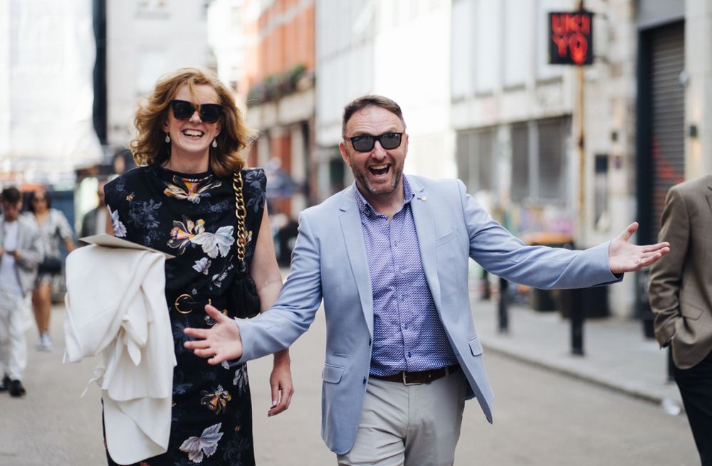 Stylishly dressed wedding guests walking and laughing on urban street.