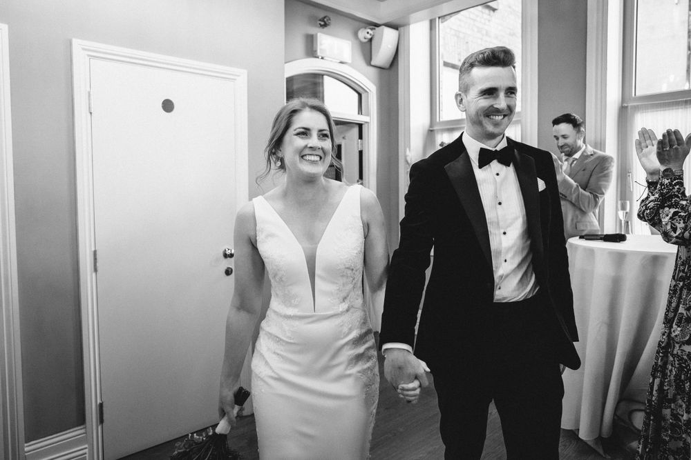 Newlyweds in formal attire walking together through doorway at venue.