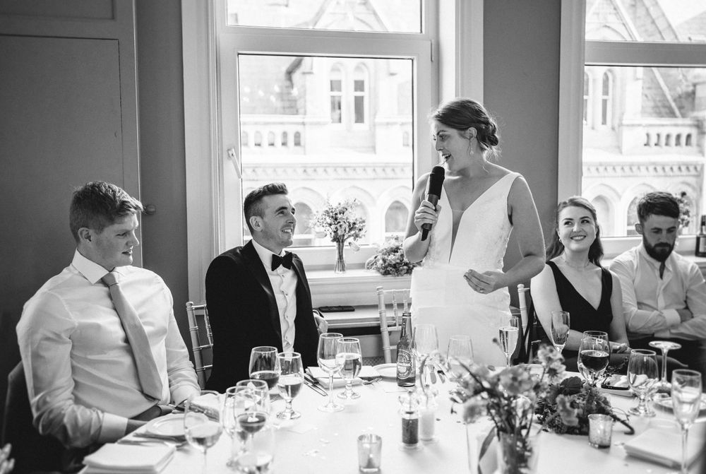 Wedding reception scene with guests seated at decorated table during speeches.