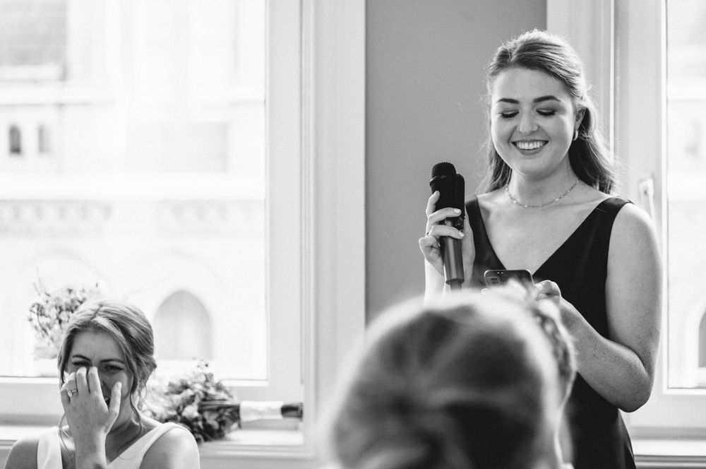 Black and white candid photo showing joyful moments during wedding reception speeches.