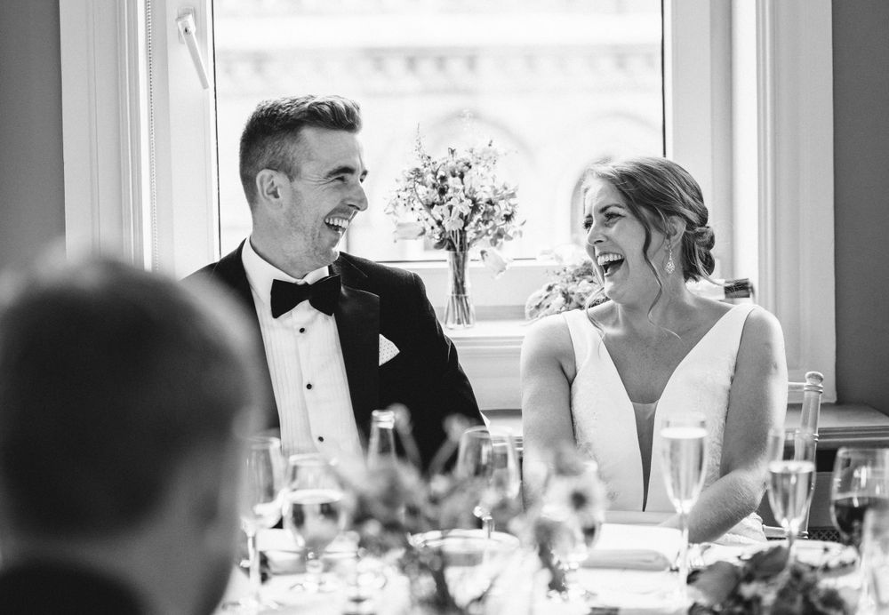 Elegant black and white photo of newlyweds laughing during wedding reception.