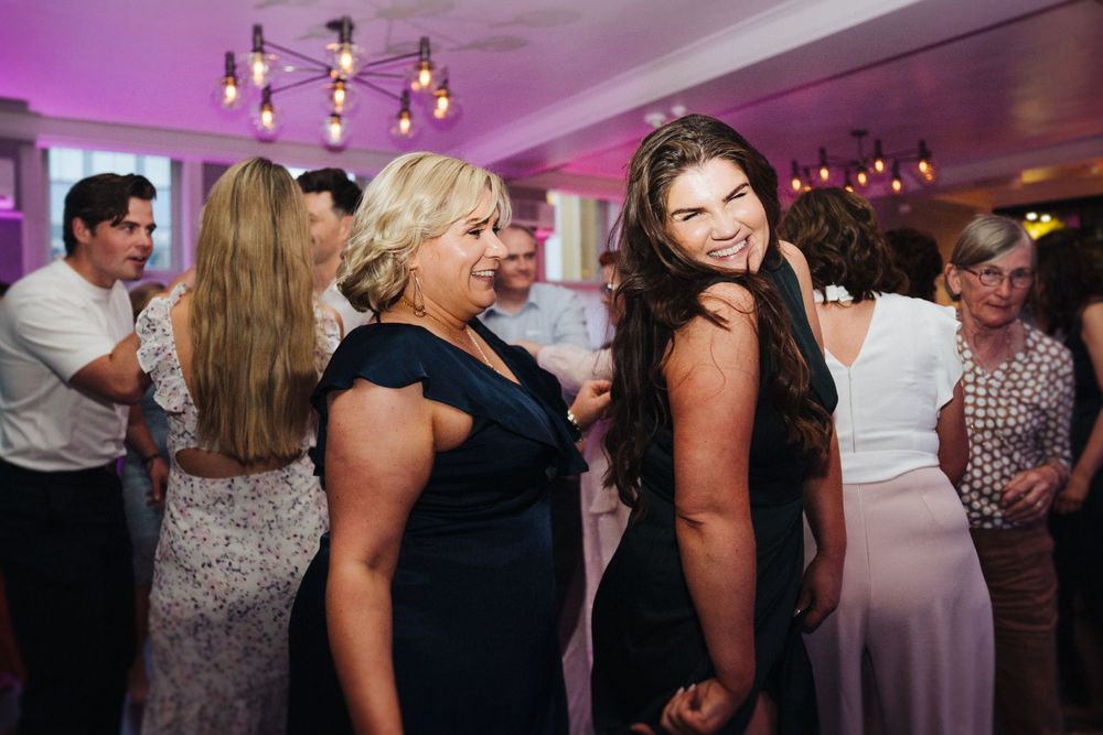 Wedding guests dancing and celebrating in purple-lit reception venue.