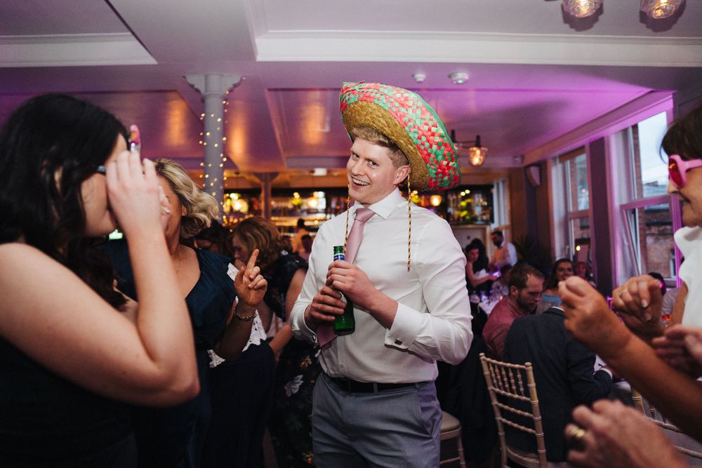 Party guest wearing a festive hat dancing at a celebration with purple ambient lighting.