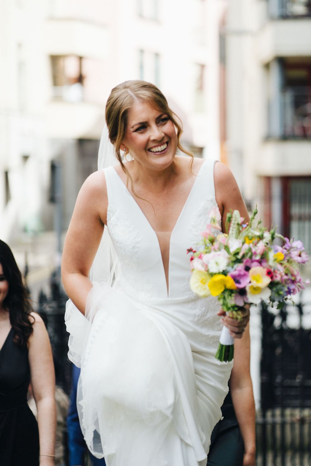 A joyful moment captured in front of urban buildings with a stunning white bridal gown and colorful bouquet.