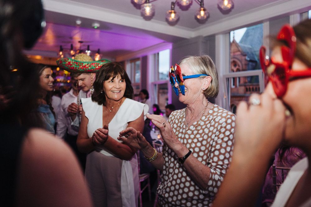 Party guests enjoying a lively celebration under pink lighting and decorative chandeliers.