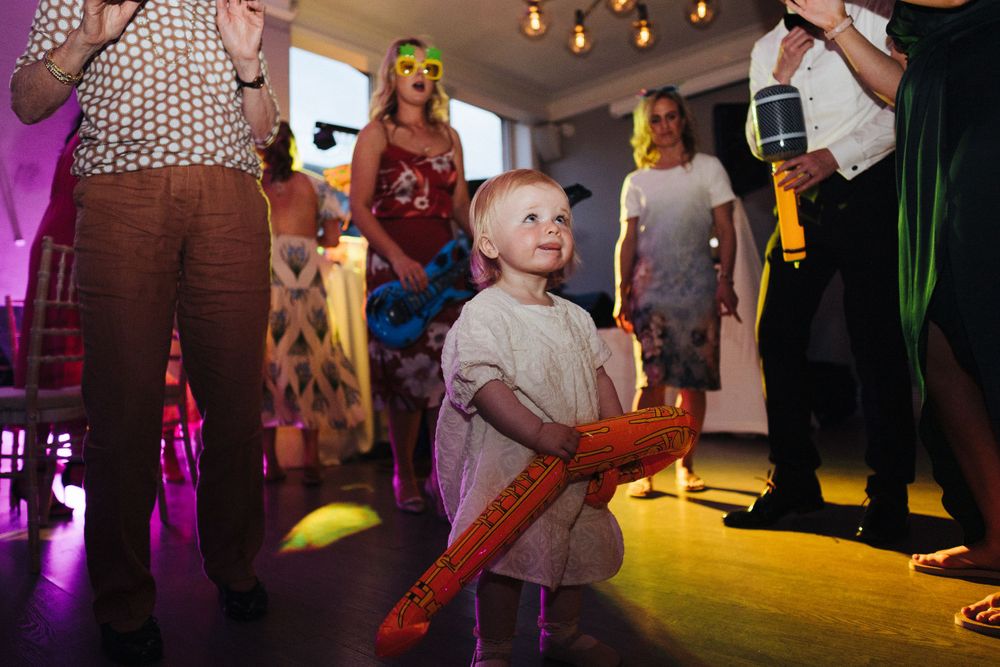 Young child with light-up toy enjoying festivities on illuminated dance floor surrounded by adults.