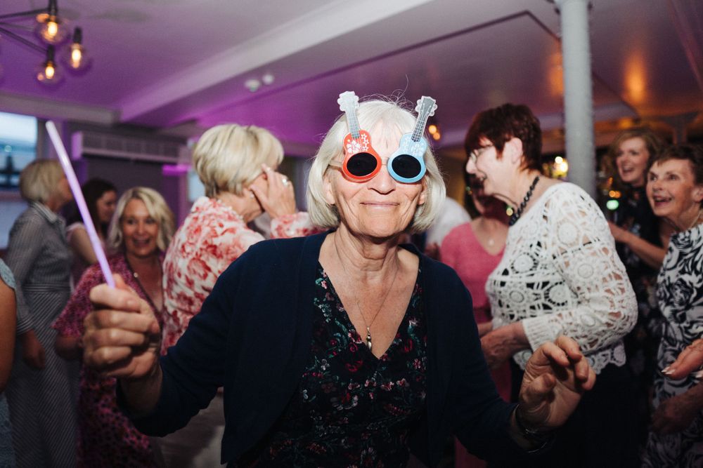 Energetic party guest wearing novelty sunglasses and holding glow sticks on a vibrant dance floor.