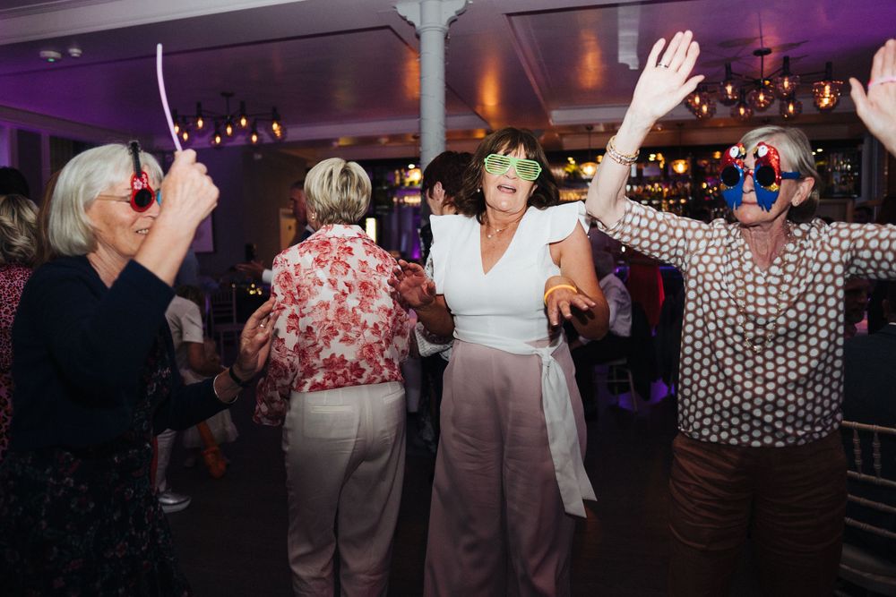 Group of guests dancing joyfully under purple mood lighting at an indoor celebration.