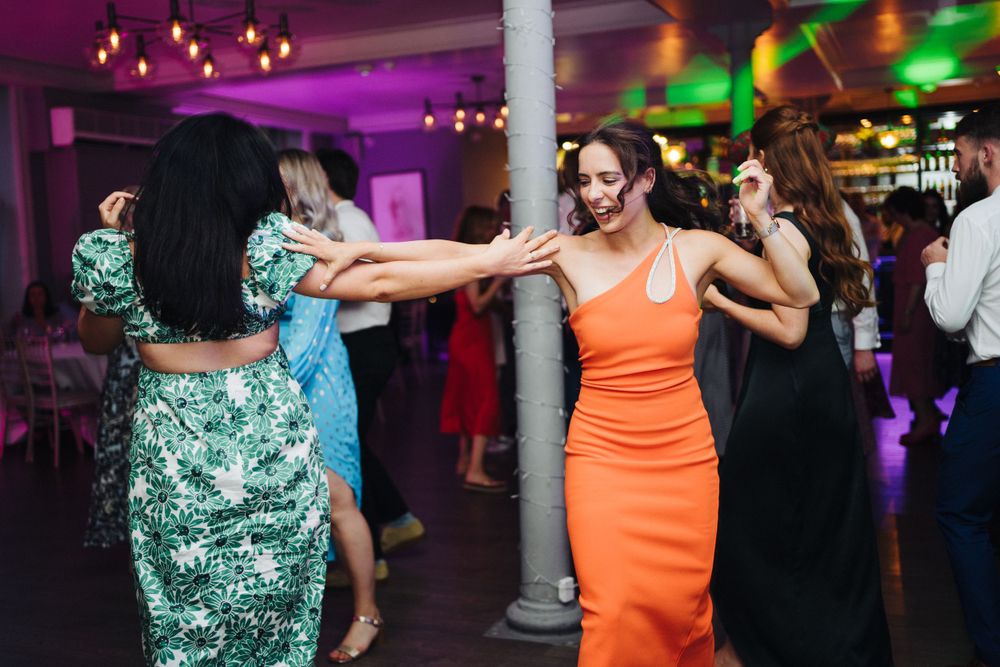 Wedding guests dance energetically on a colorful dance floor with purple and green lighting at a reception celebration.