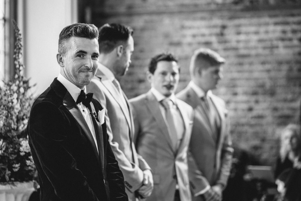 Groomsmen lined up at wedding ceremony against rustic brick wall background.