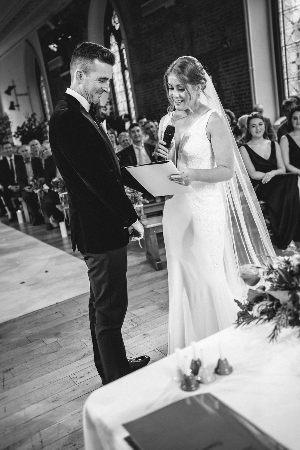 Black and white wedding ceremony photo in rustic venue with wooden floors and brick walls.
