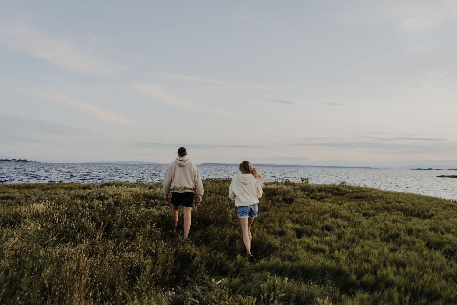 Two people walking on a grassy coastal path overlooking the ocean at dusk.