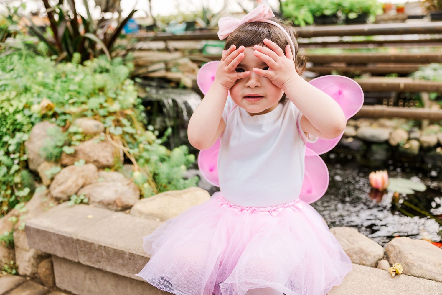 Playful child in fairy costume covers eyes while playing peek-a-boo outdoors.