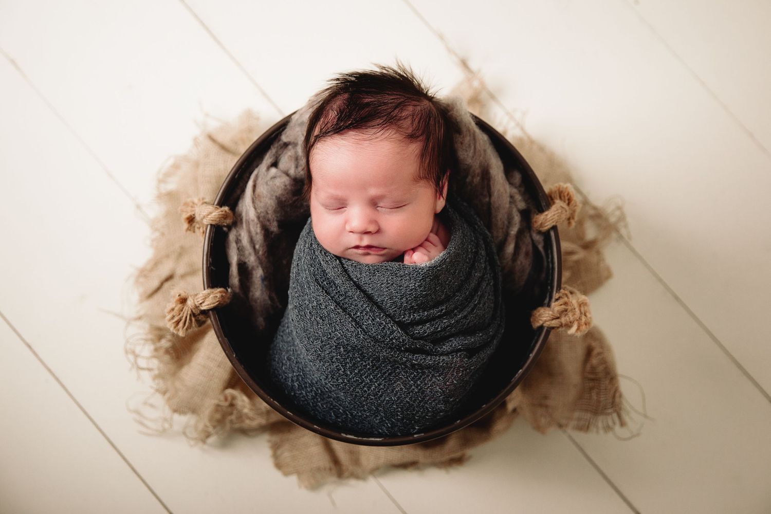 infant boy in galvanized bucket prop on white wood floor