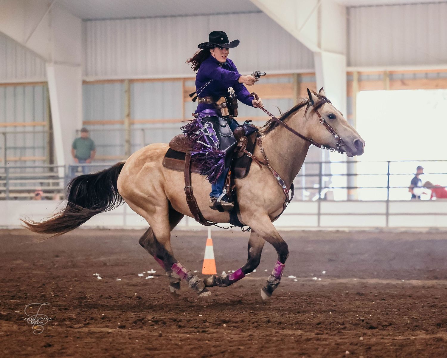 A cowgirl riding a quarter horse buckskin during cowboy mounted shooting competition.