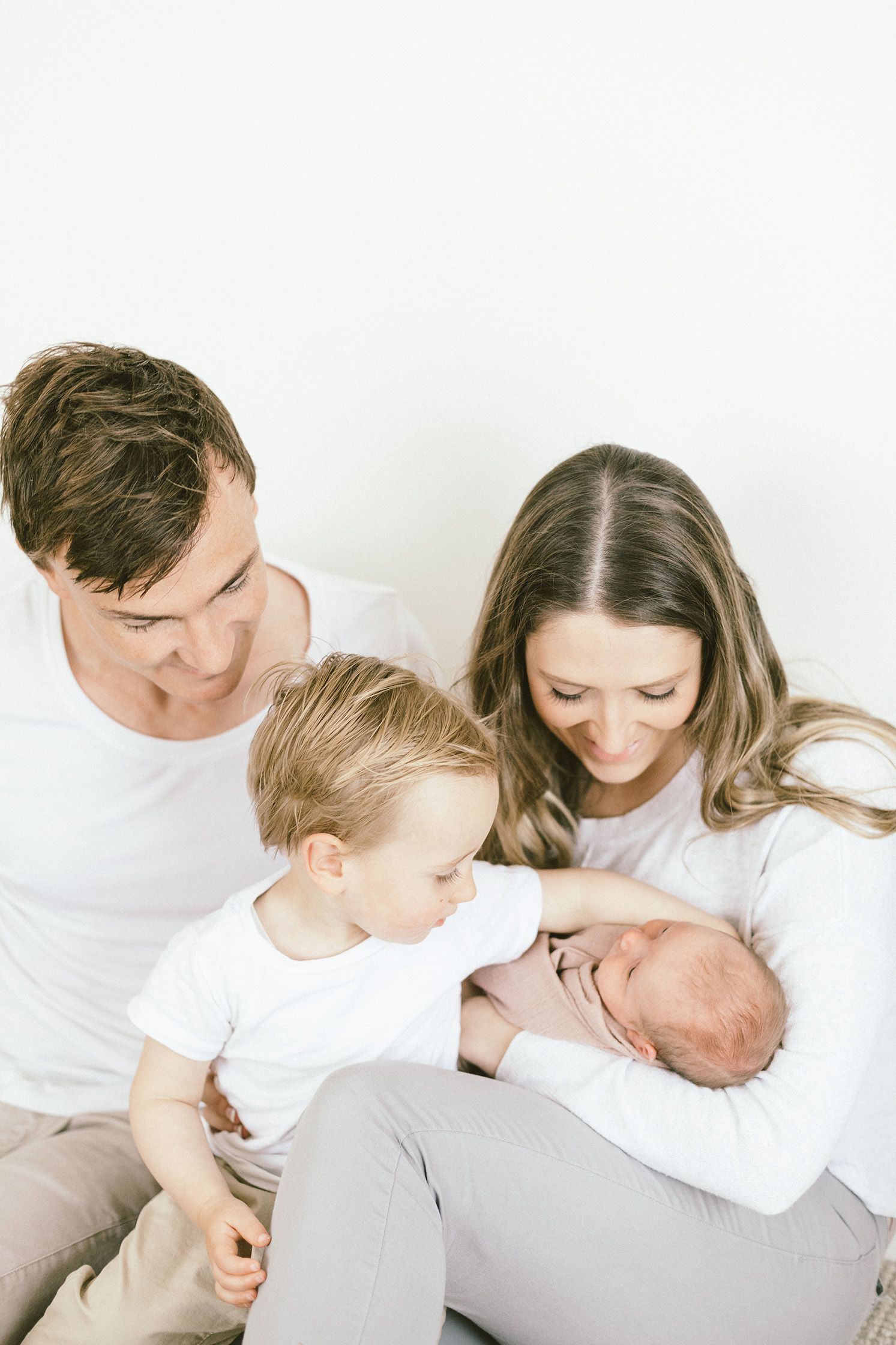 Family gathering close together on white background for newborn portraits.