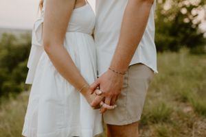 Close-up of couple holding hands outdoors wearing white and khaki summer outfits.