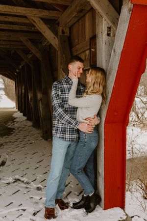 A romantic winter moment between a couple in a covered bridge with snow on the ground.