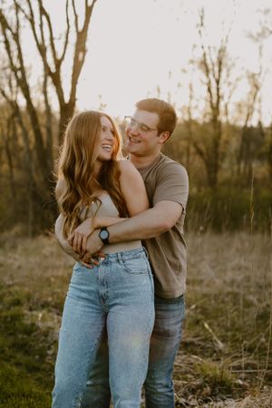 Happy couple laughing while embracing in casual attire during golden hour photoshoot.