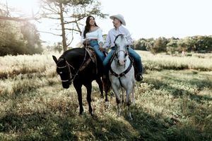 Couple riding horses together through a sun-drenched meadow at sunset.
