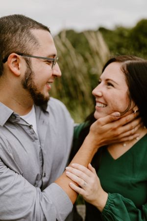 Couple sharing intimate moment outdoors with engagement ring visible.