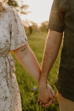 Close-up of couple holding hands showing delicate floral dress and casual attire.