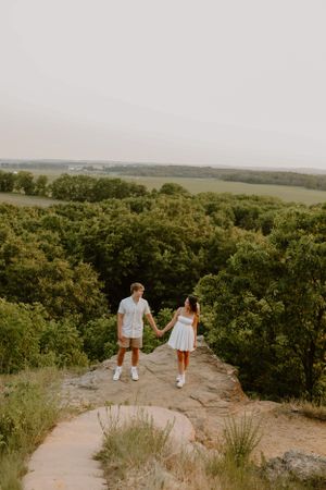 A couple in white outfits holding hands while standing on a scenic overlook.