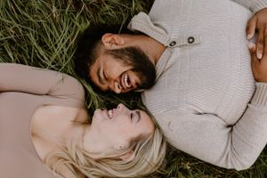 A couple lying in grass sharing a playful moment together.