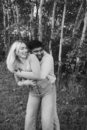 A joyful couple embracing and laughing together in a birch forest.
