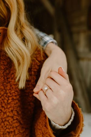Close-up of an engagement ring on a hand against an orange sweater background.